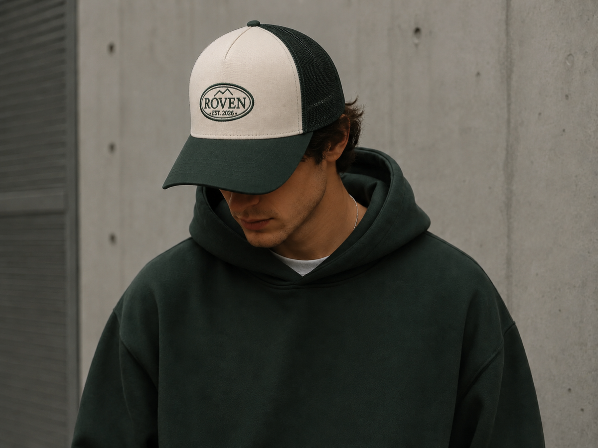 Person mit ROVEN Cap in Grün und grünem Hoodie vor einer Betonwand